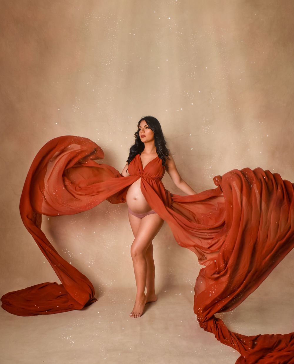 Artistic maternity photo with flowing red fabric against neutral backdrop.