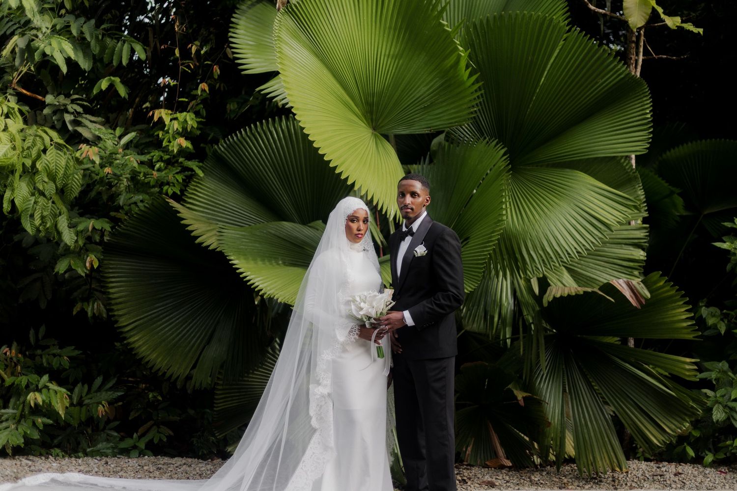 A couple poses in a lush green garden setting with natural lighting.