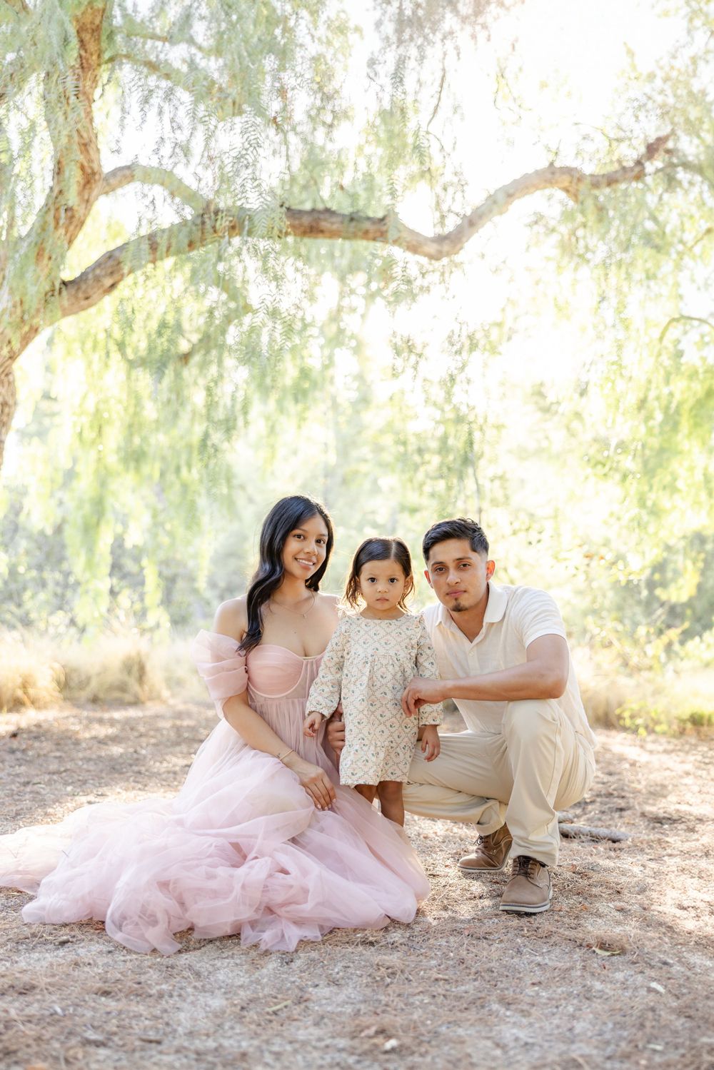 Family in coordinated outfits enjoying a tender moment together in a sun-dappled outdoor setting.