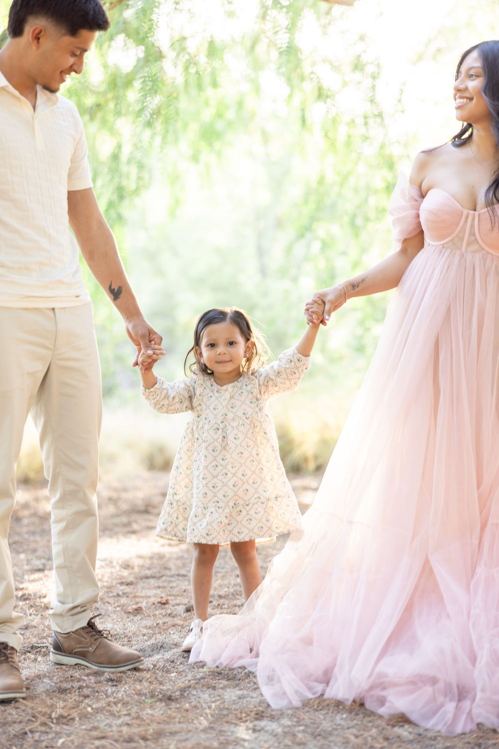 Family in coordinated pink and white outfits dancing together under willow trees.