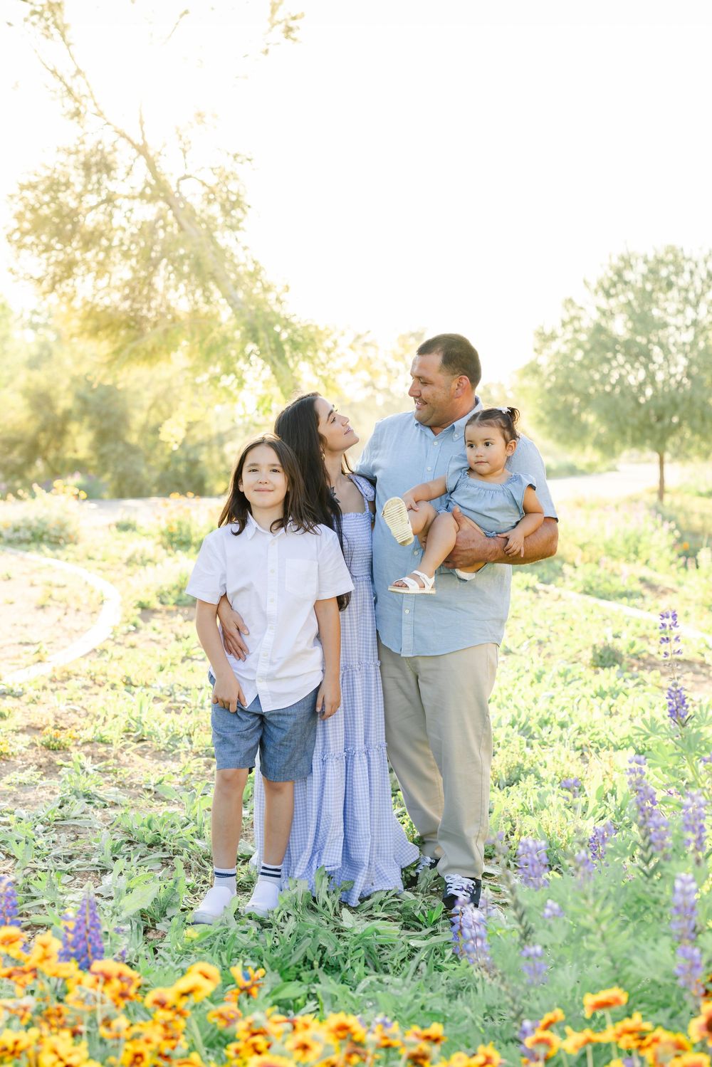 Family of three sharing joyful moments among wildflowers and sunflowers.