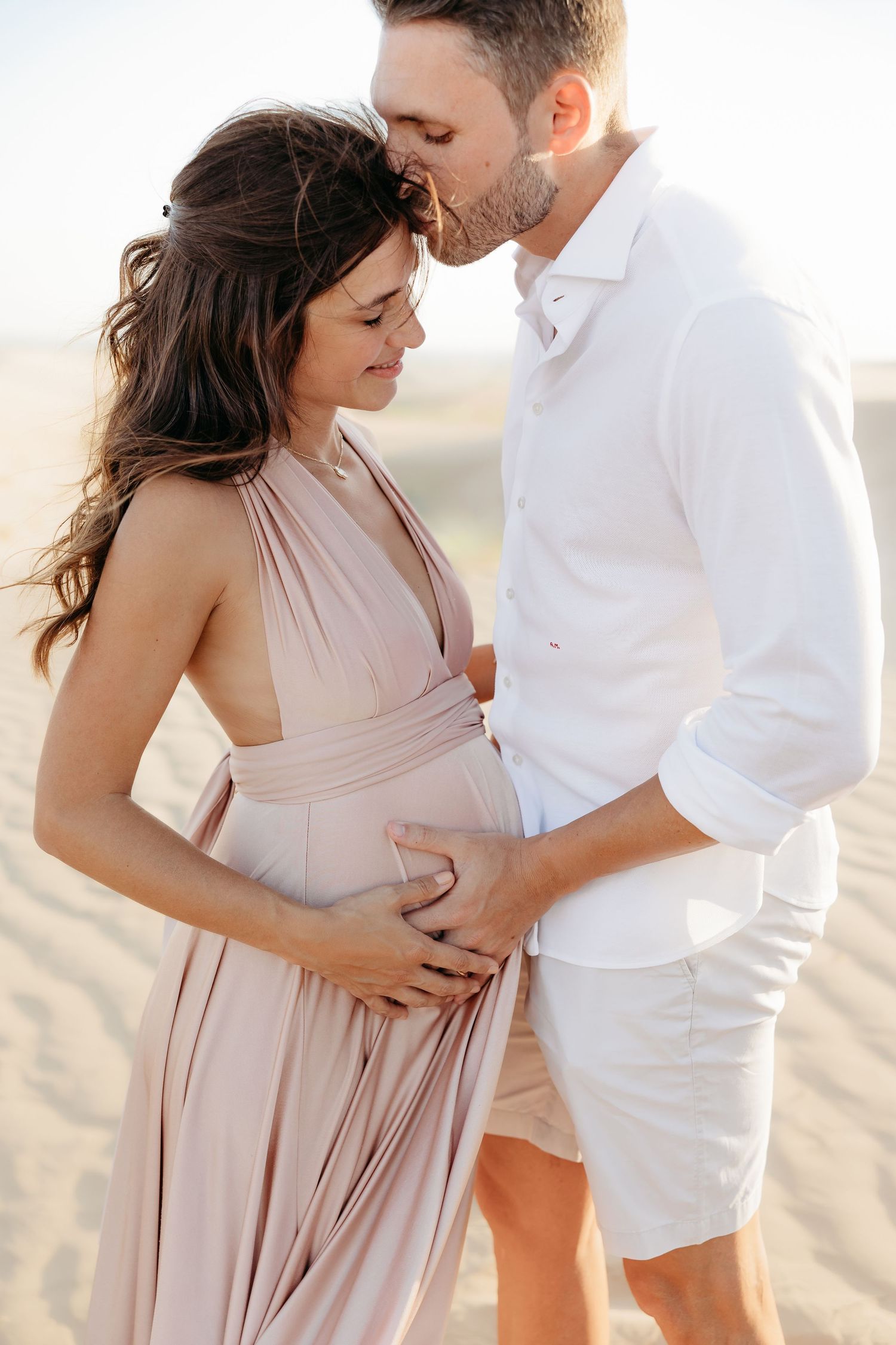 A romantic maternity moment of a couple, with the man gently embracing the woman as she holds her baby bump.