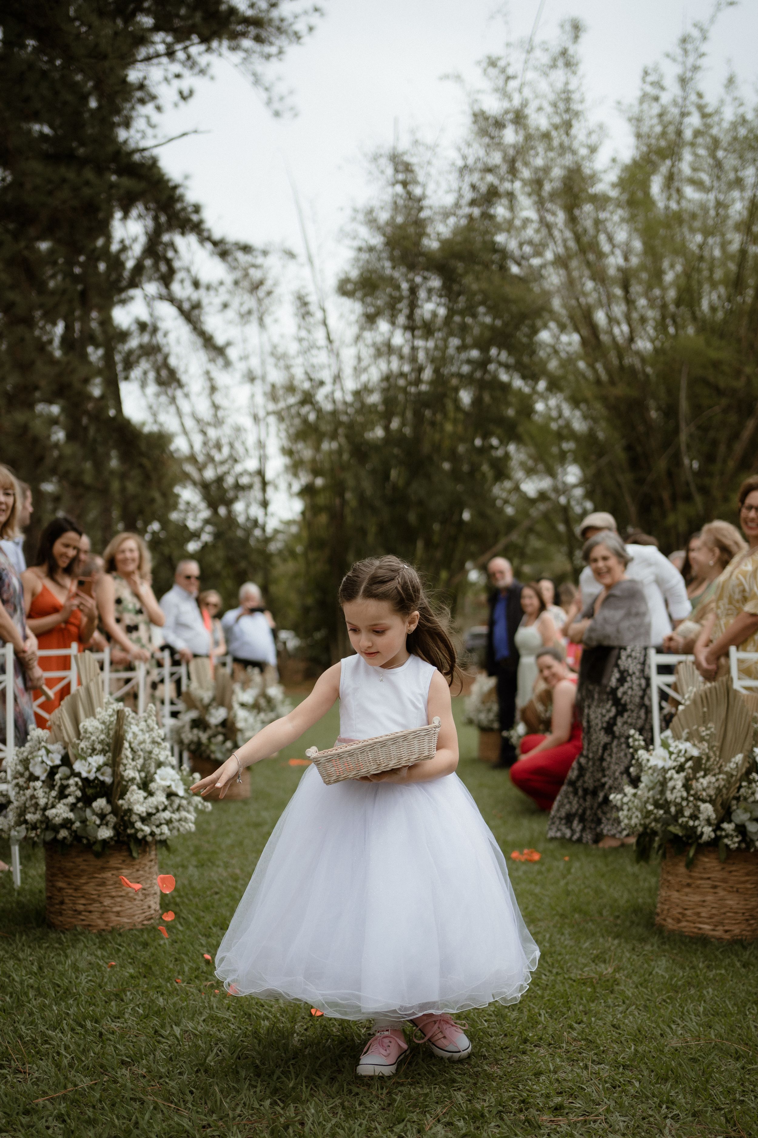 Young flower girls in white dresses dance and twirl on grass during outdoor wedding ceremony.