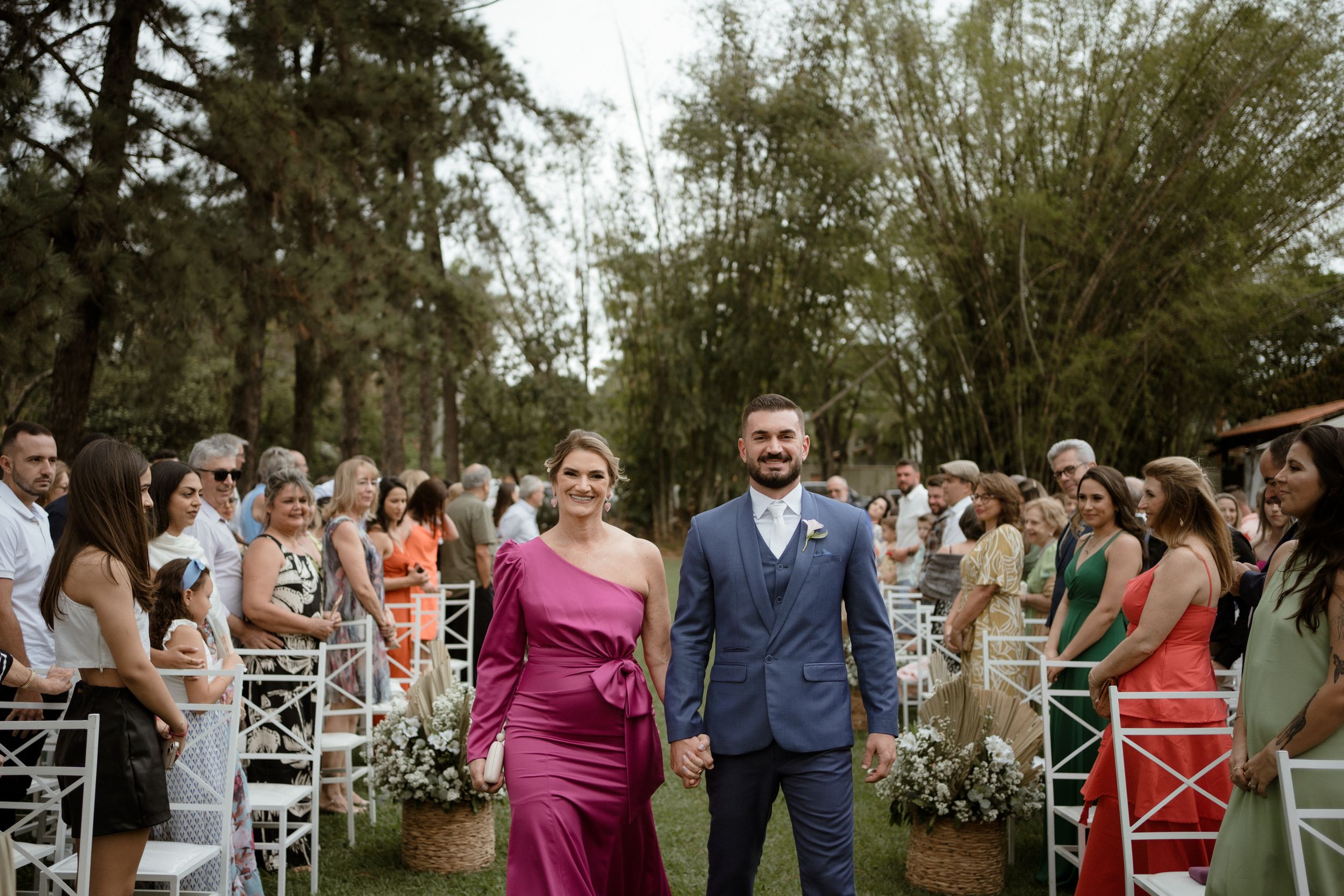 Wedding ceremony recessional on a garden path lined with white chairs and floral arrangements.