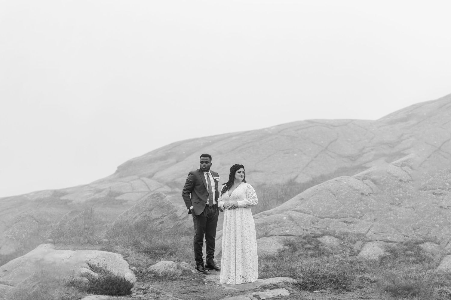 Black and white photo of newlyweds standing together on a rocky mountainous landscape.