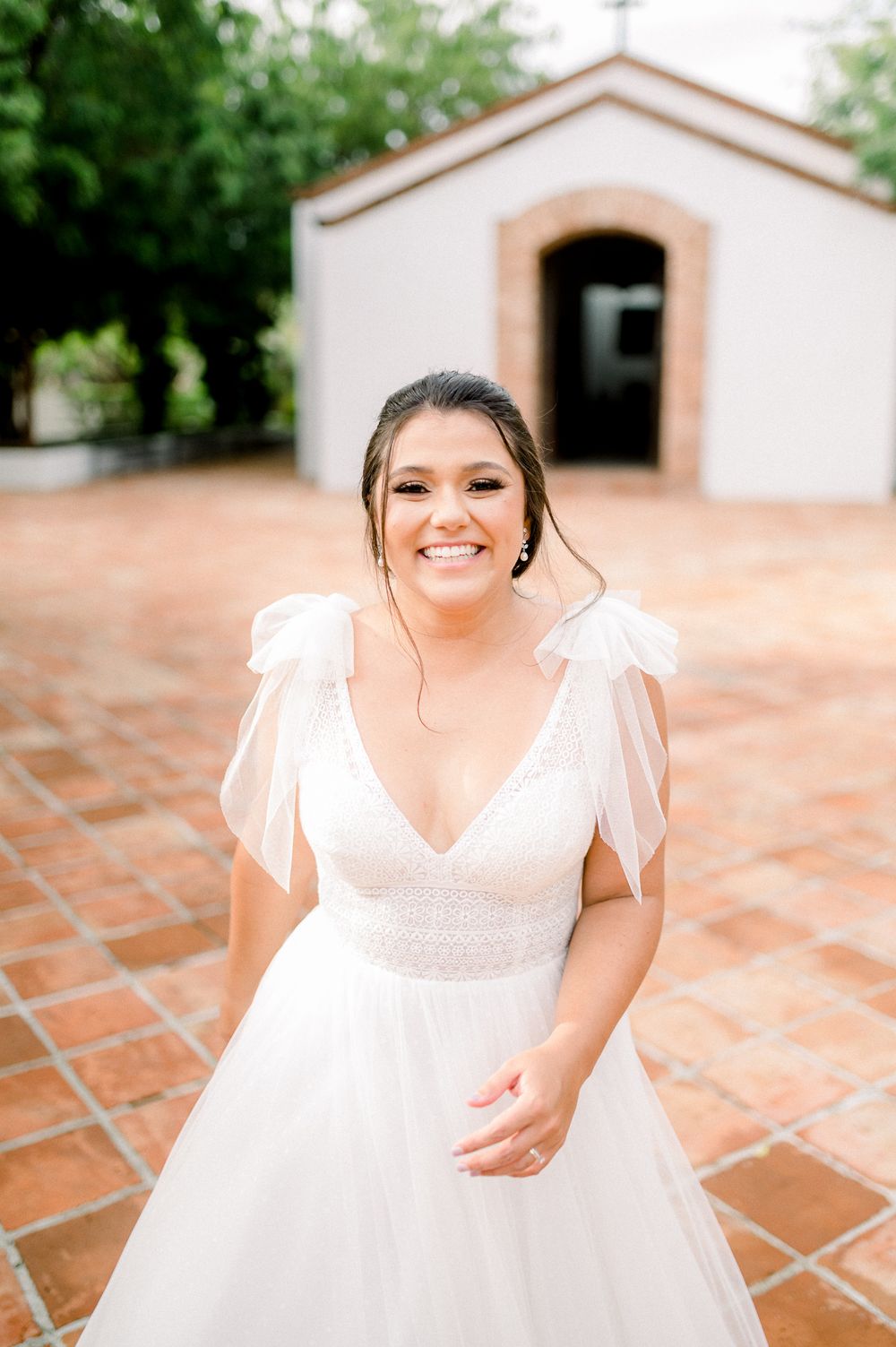 Bride in white V-neck wedding dress poses in front of small chapel.