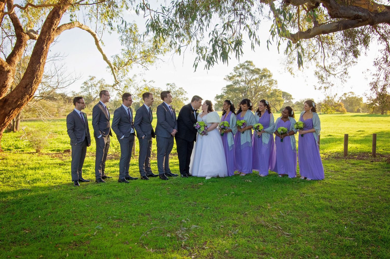 bridal party in grey and purple smiling at bride and groom