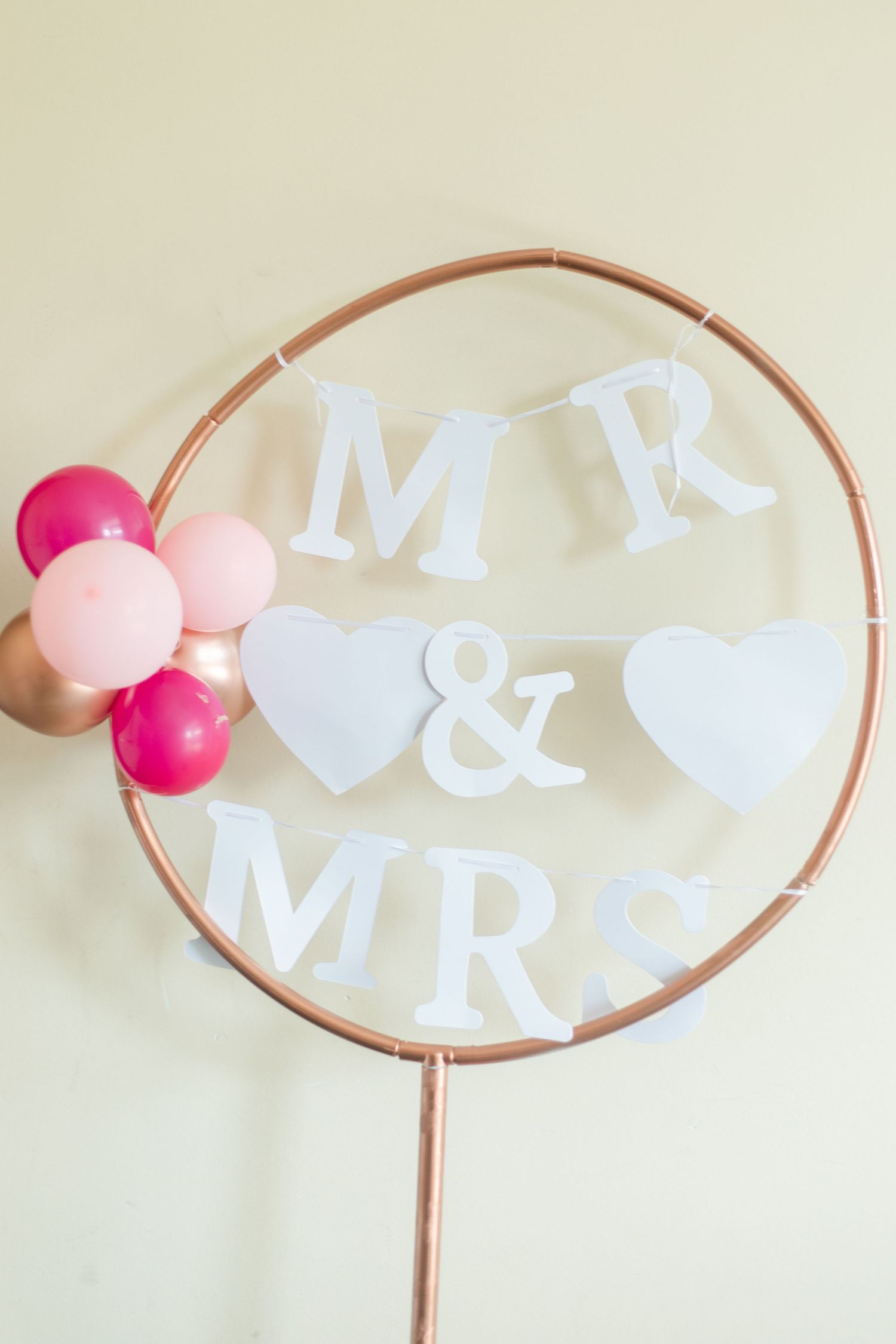 Copper hoop wedding decor with white letters and pink pom poms creating a modern minimalist design.