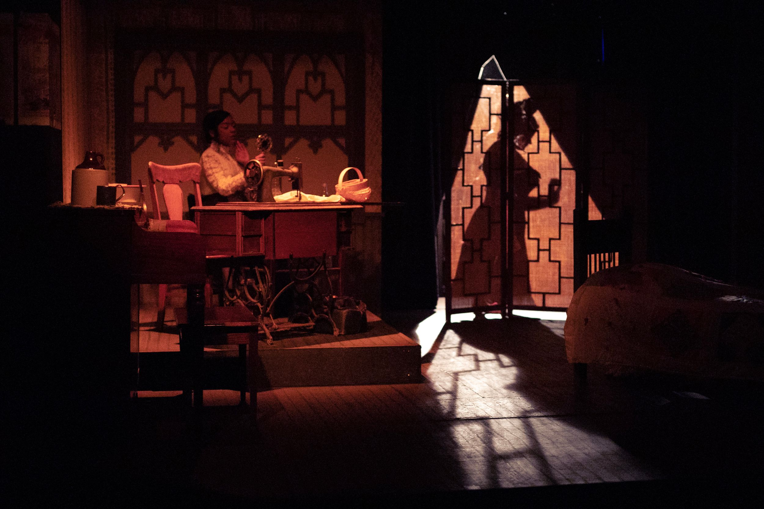 Dark atmospheric stage scene with dramatic lighting casting shadows through a gothic doorway.