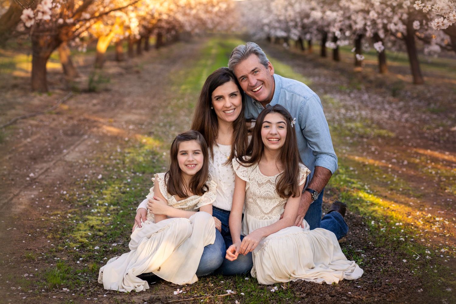 Family portrait in a blooming orchard during golden sunset hour.