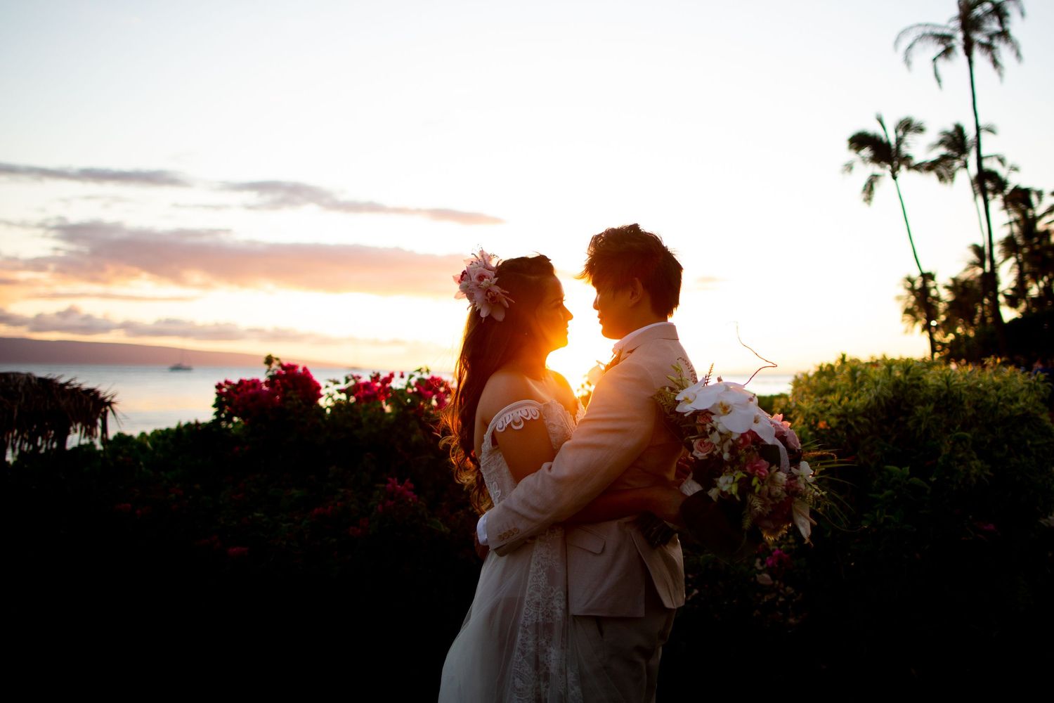 A couple shares an intimate moment at sunset with palm trees silhouetted in the background.