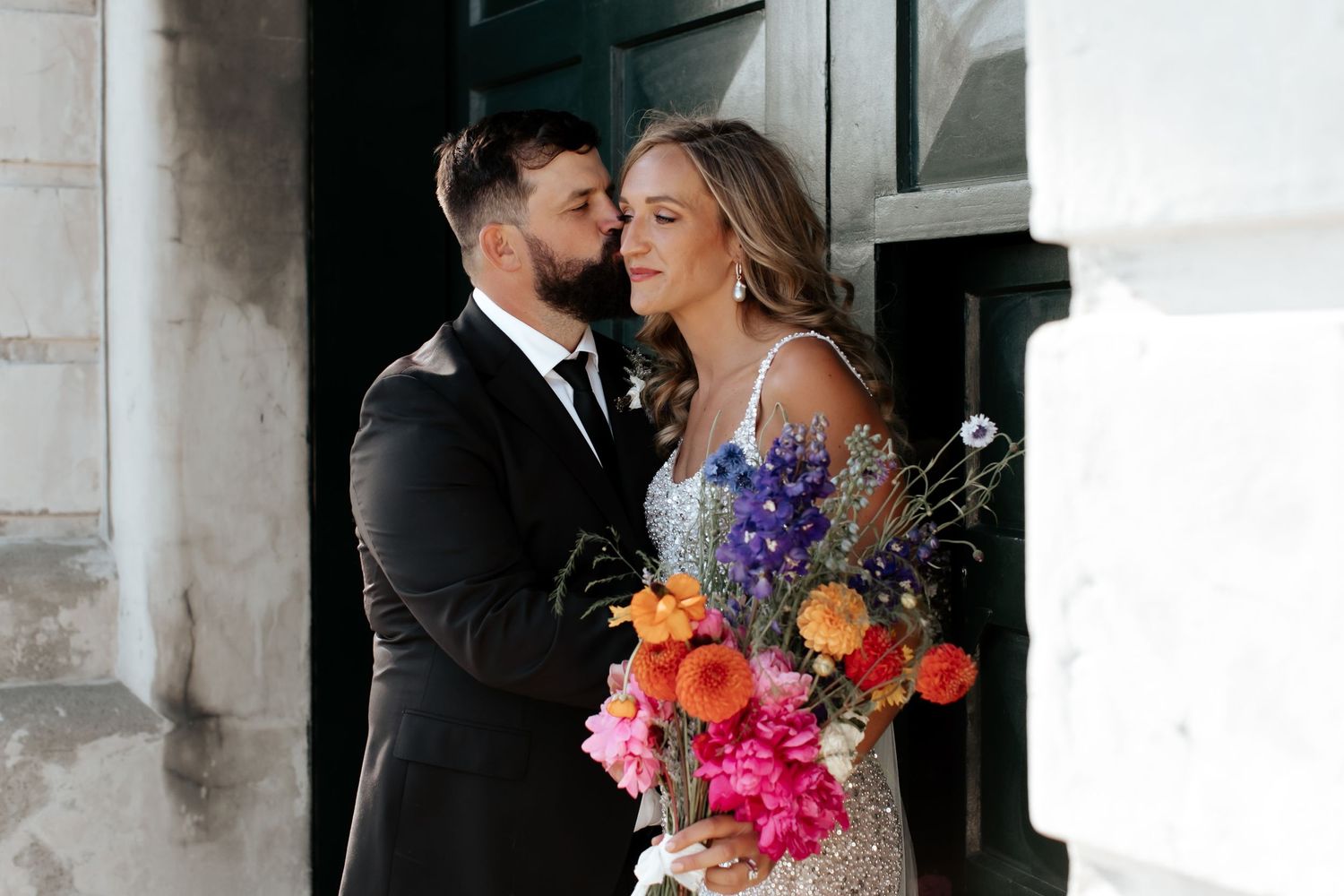 An intimate moment between newlyweds with a vibrant floral bouquet against an industrial backdrop.