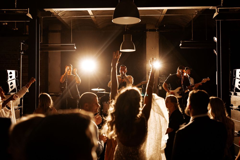 Concert crowd silhouetted against bright stage lights while band performs live music.