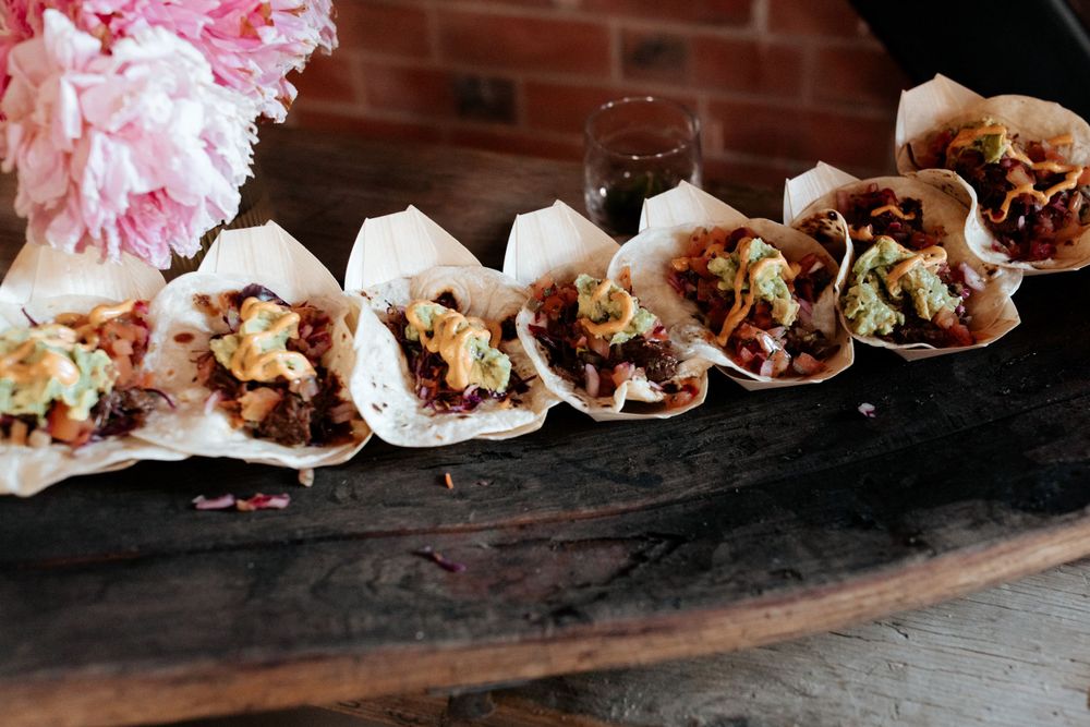 Row of street-style tacos displayed on rustic wooden serving board.