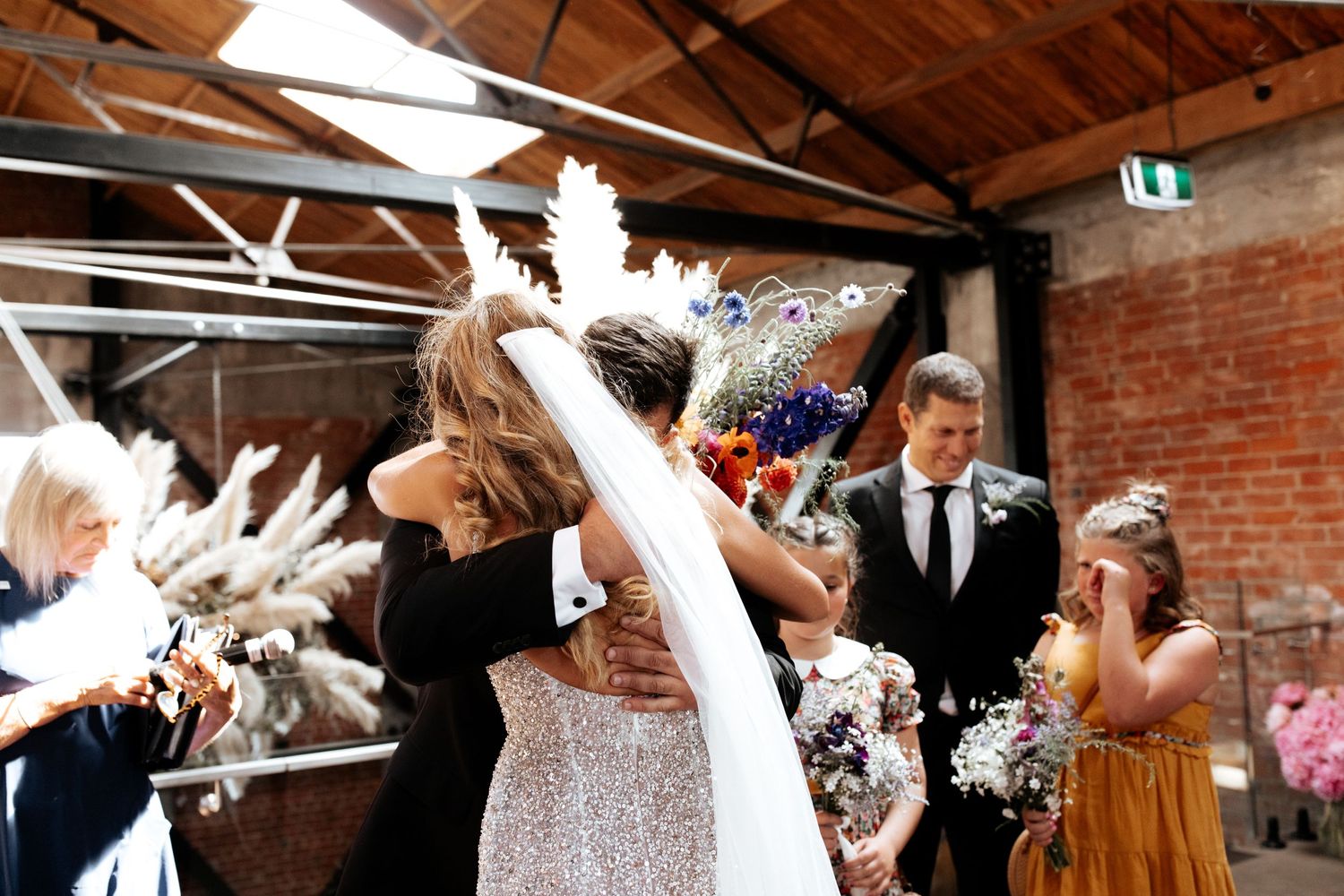 Wedding celebration in industrial venue with pampas grass decor as guests shower newlyweds with confetti.