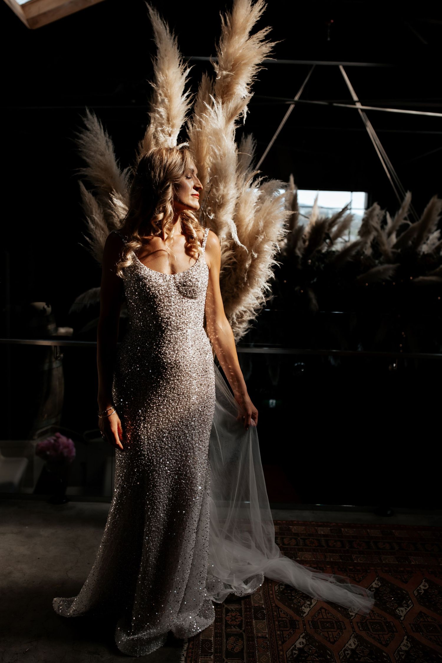 A stunning sparkly wedding dress with dramatic pampas grass decorations in a moody dark setting.