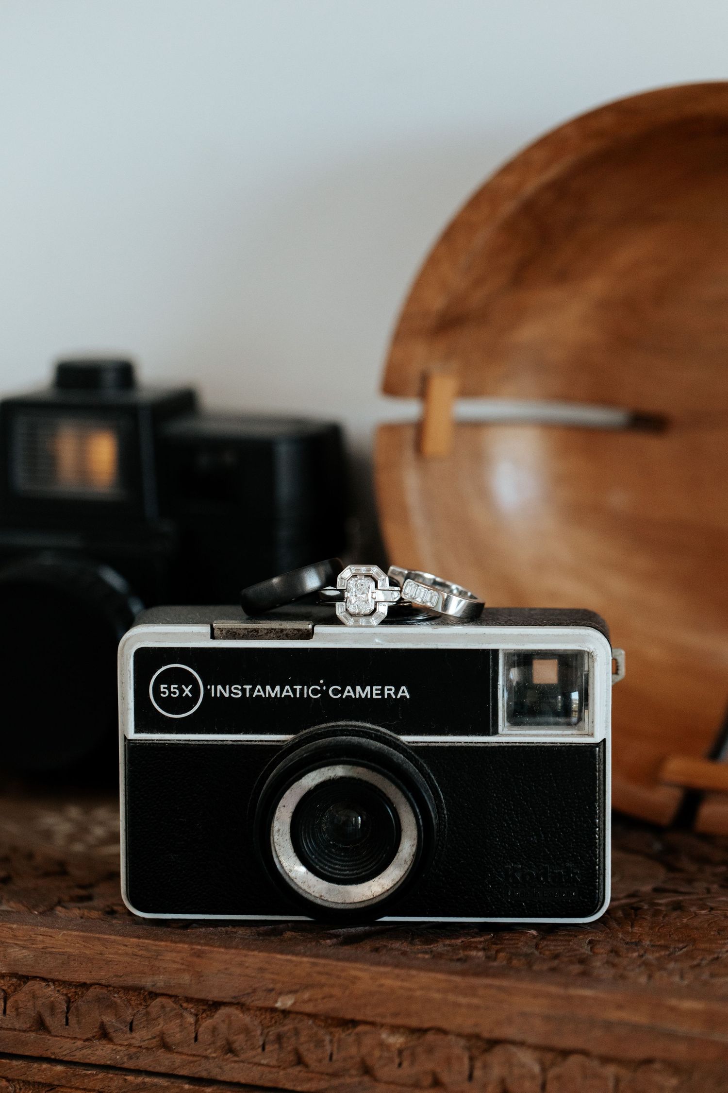A vintage Instamatic camera with wedding rings placed on top against a wooden background.