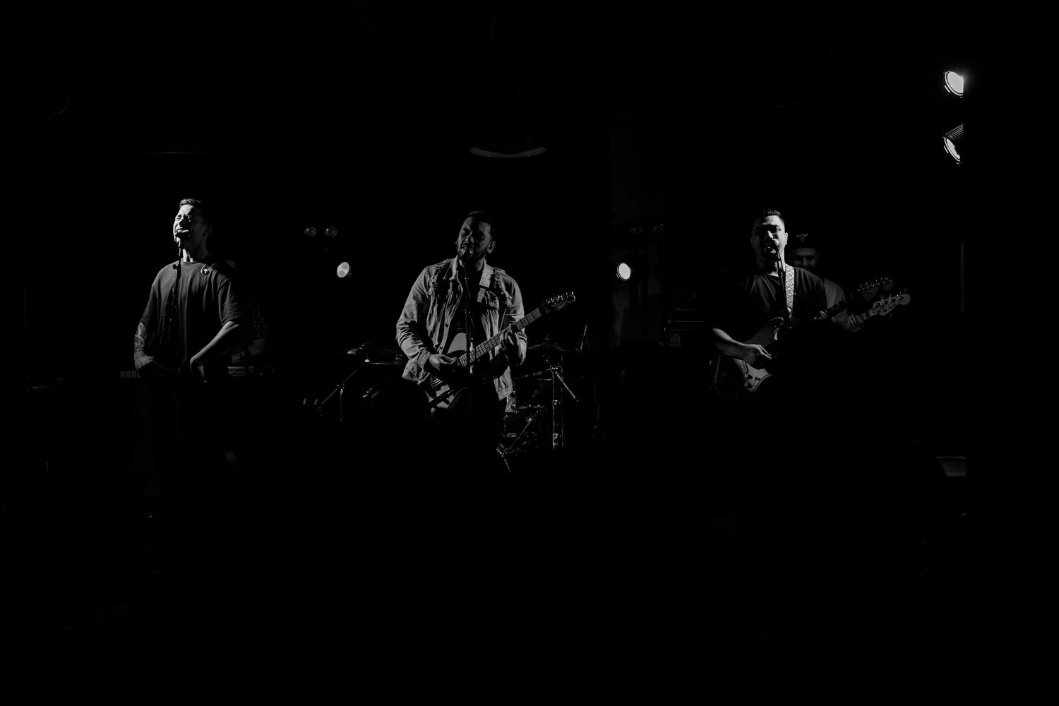 Silhouetted band members performing on a dark stage in moody black and white.
