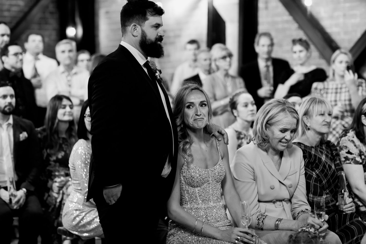 Black and white candid shot of wedding ceremony with guests seated in industrial venue.