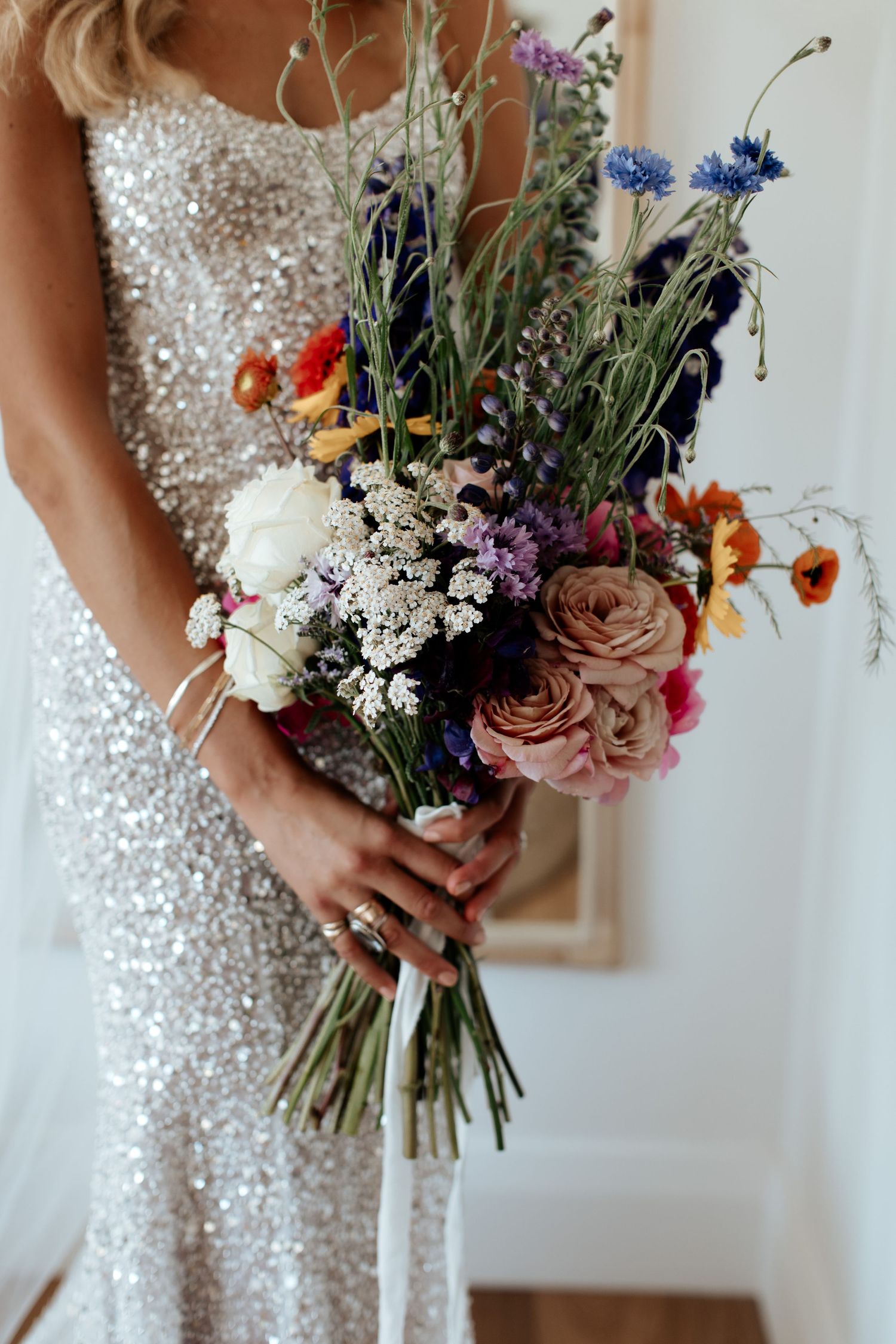 Colorful wildflower wedding bouquet held against sparkly sequined dress.