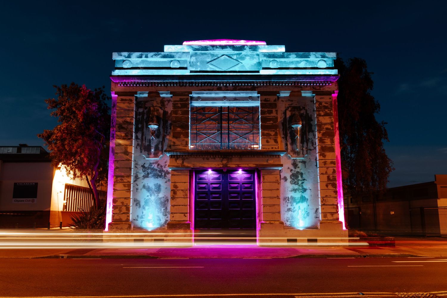 Historic building facade illuminated with colorful blue and pink lights at night.