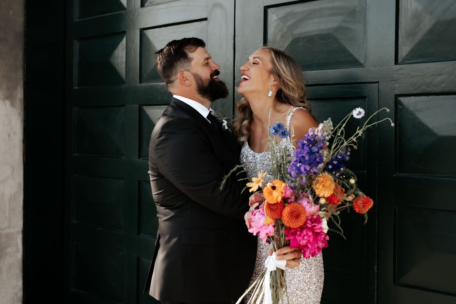 A joyful candid moment between newlyweds sharing laughter with a colorful bouquet.