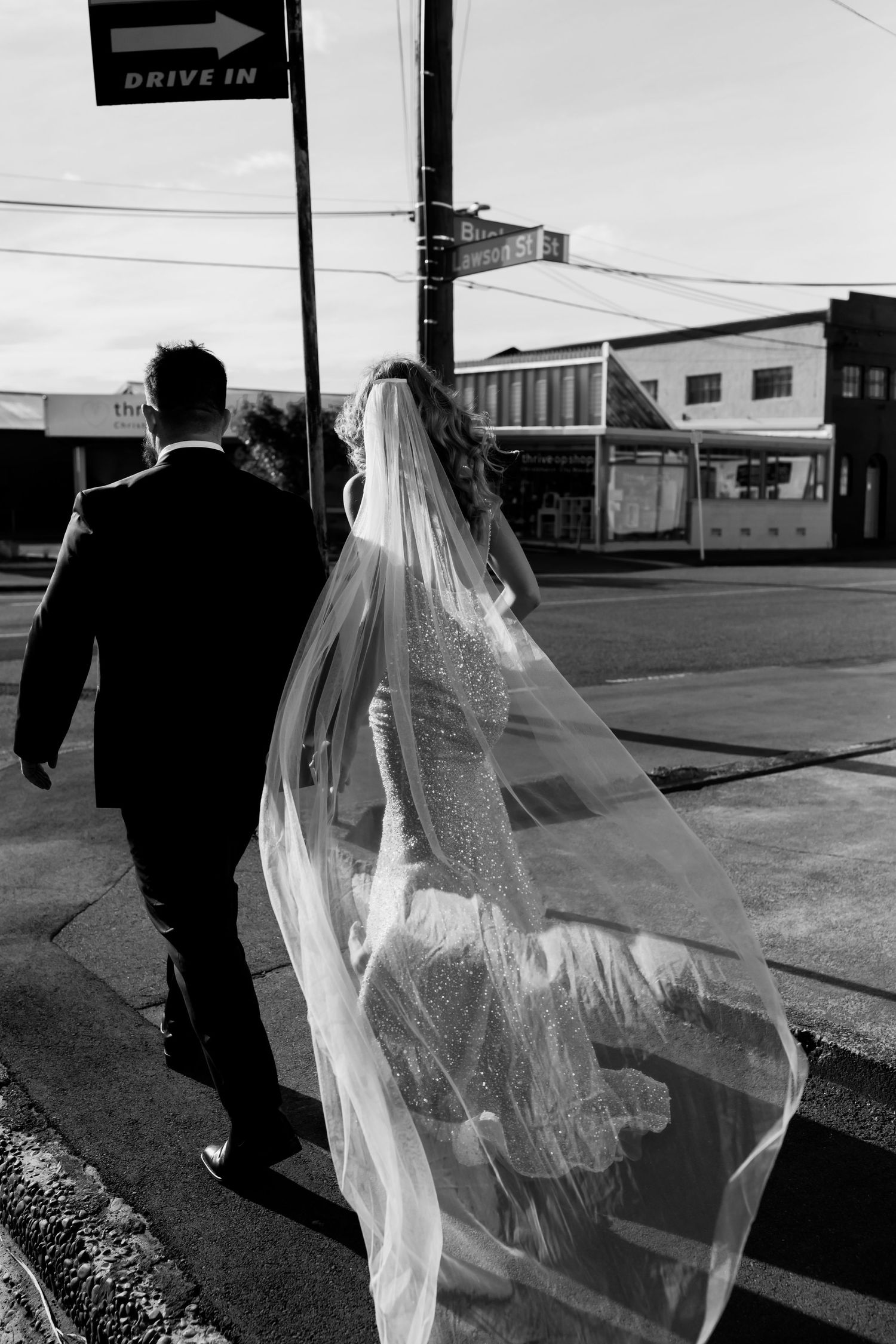 Black and white photo of newlyweds walking down urban street with flowing veil.