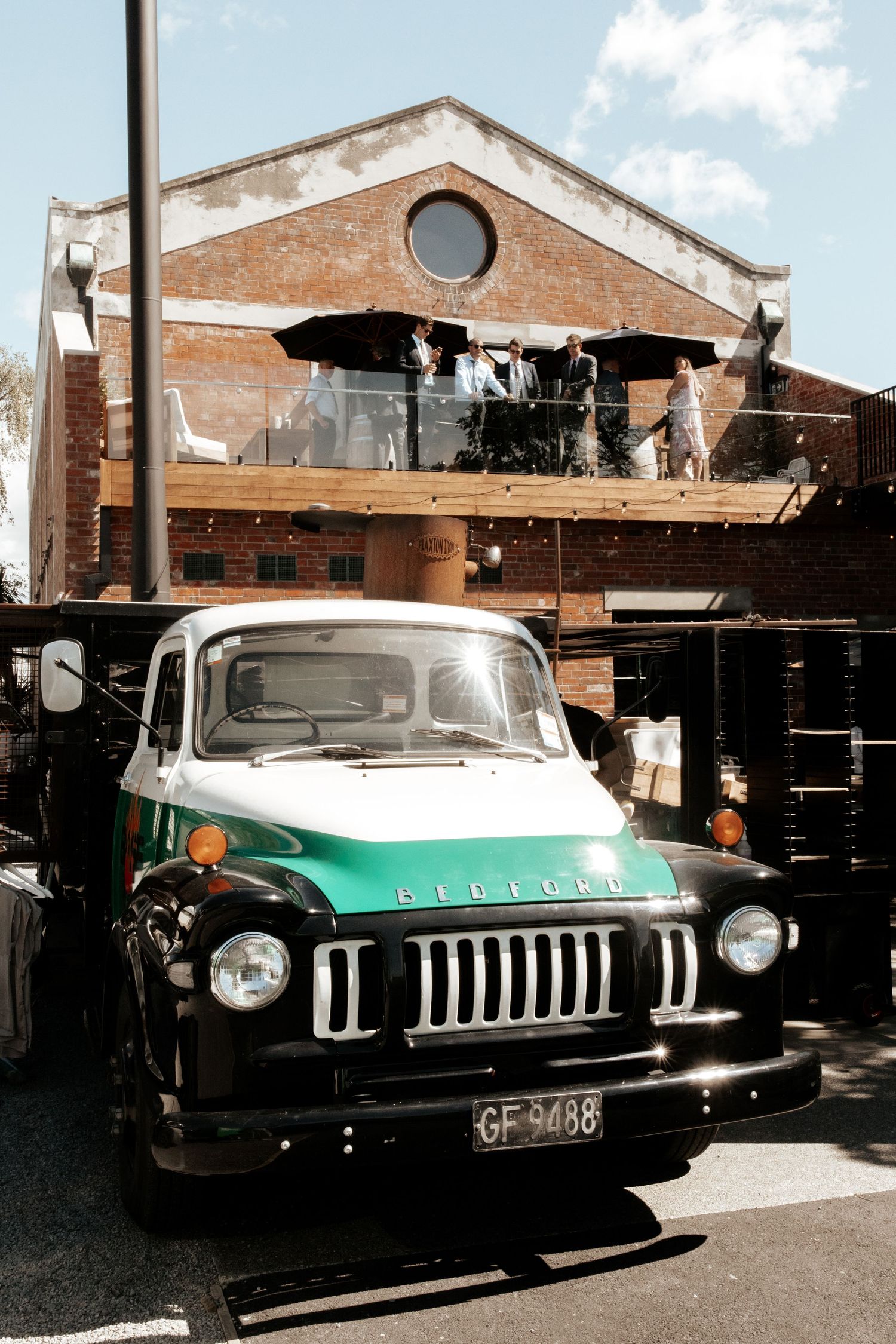 Vintage turquoise and black Bedford truck parked in front of a brick building.