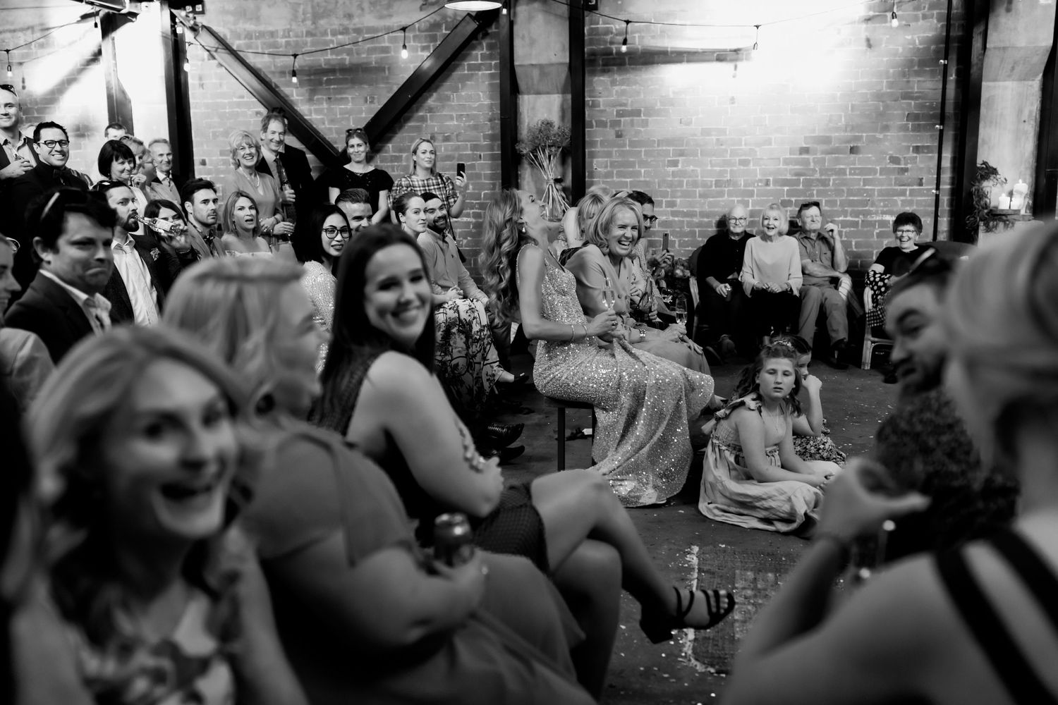 Black and white photo of wedding guests laughing and enjoying reception in industrial venue.