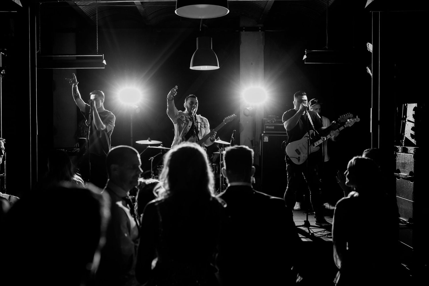 Band performing on stage with enthusiastic crowd silhouettes in the foreground.