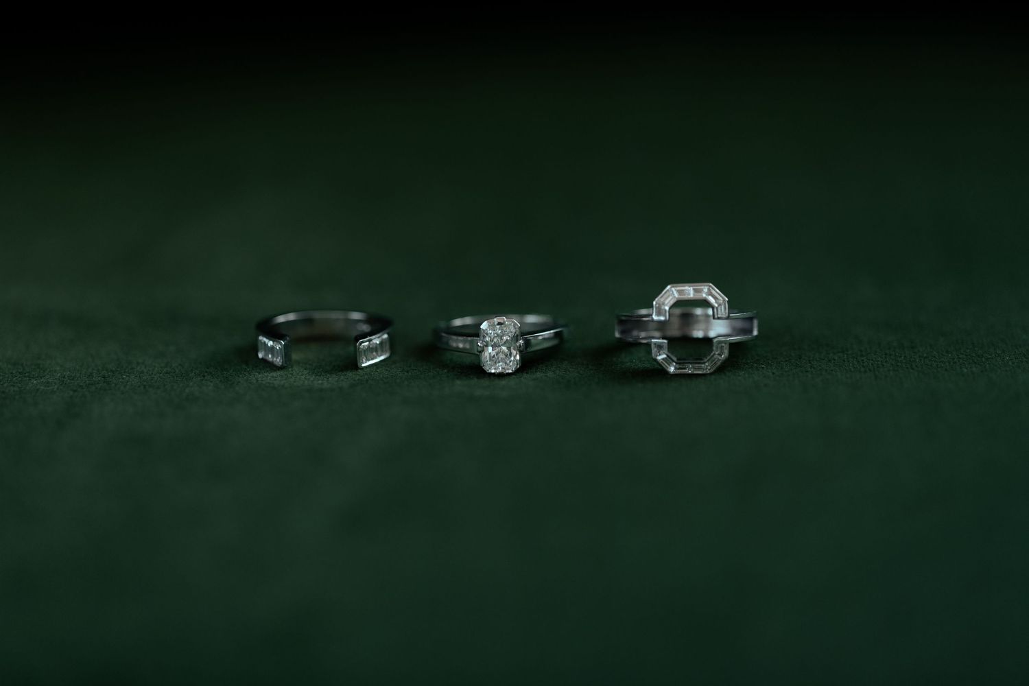 Three diamond engagement rings lined up on dark green velvet background.