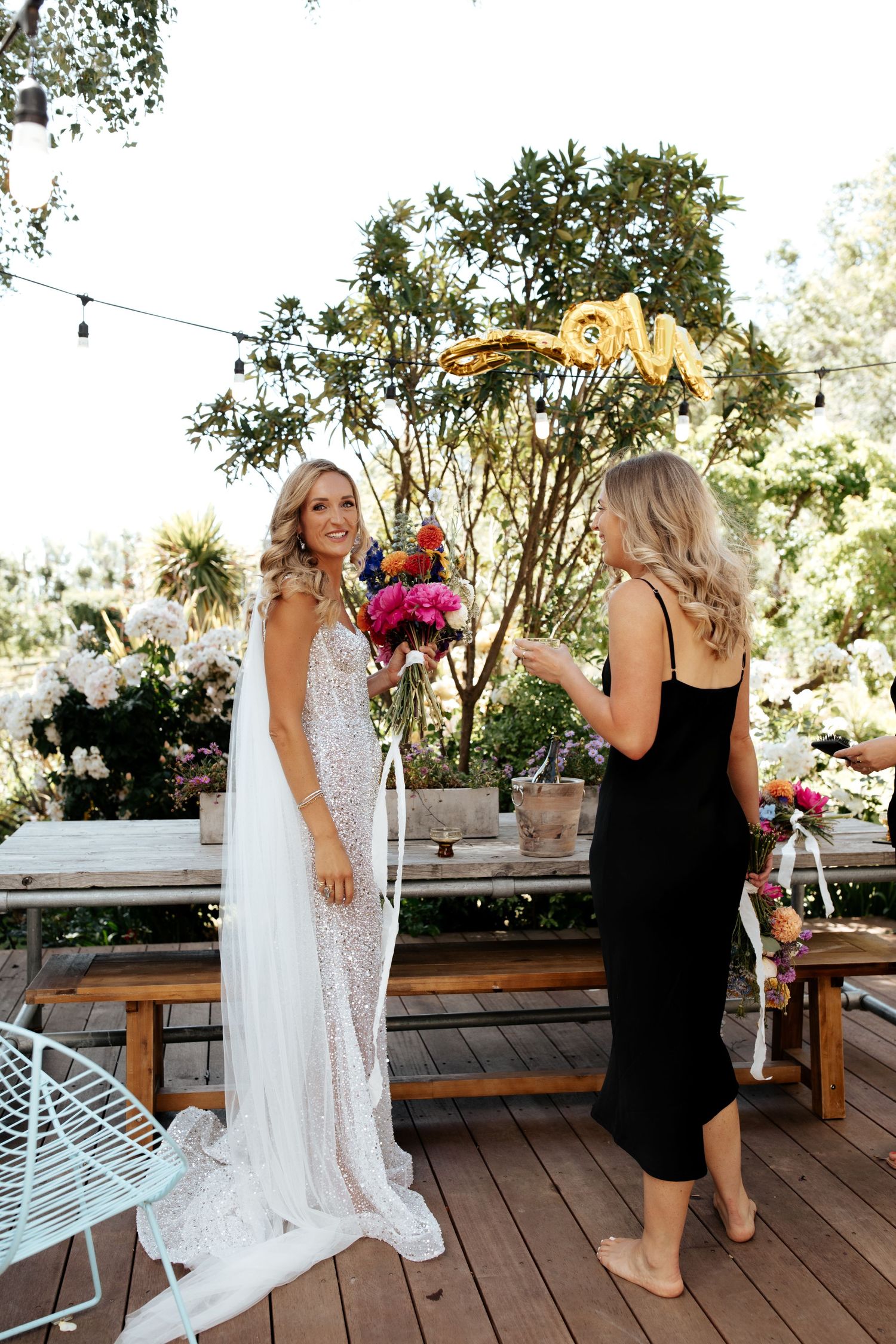 Wedding scene on outdoor deck with casual conversation and vibrant floral arrangements.