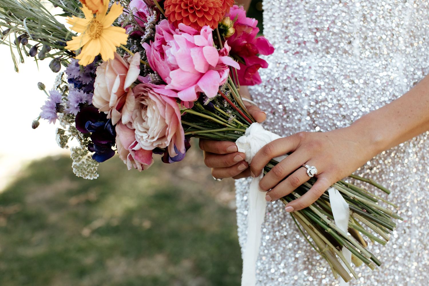 Close up of colorful bridal bouquet with pink and purple flowers held against sparkly wedding dress.