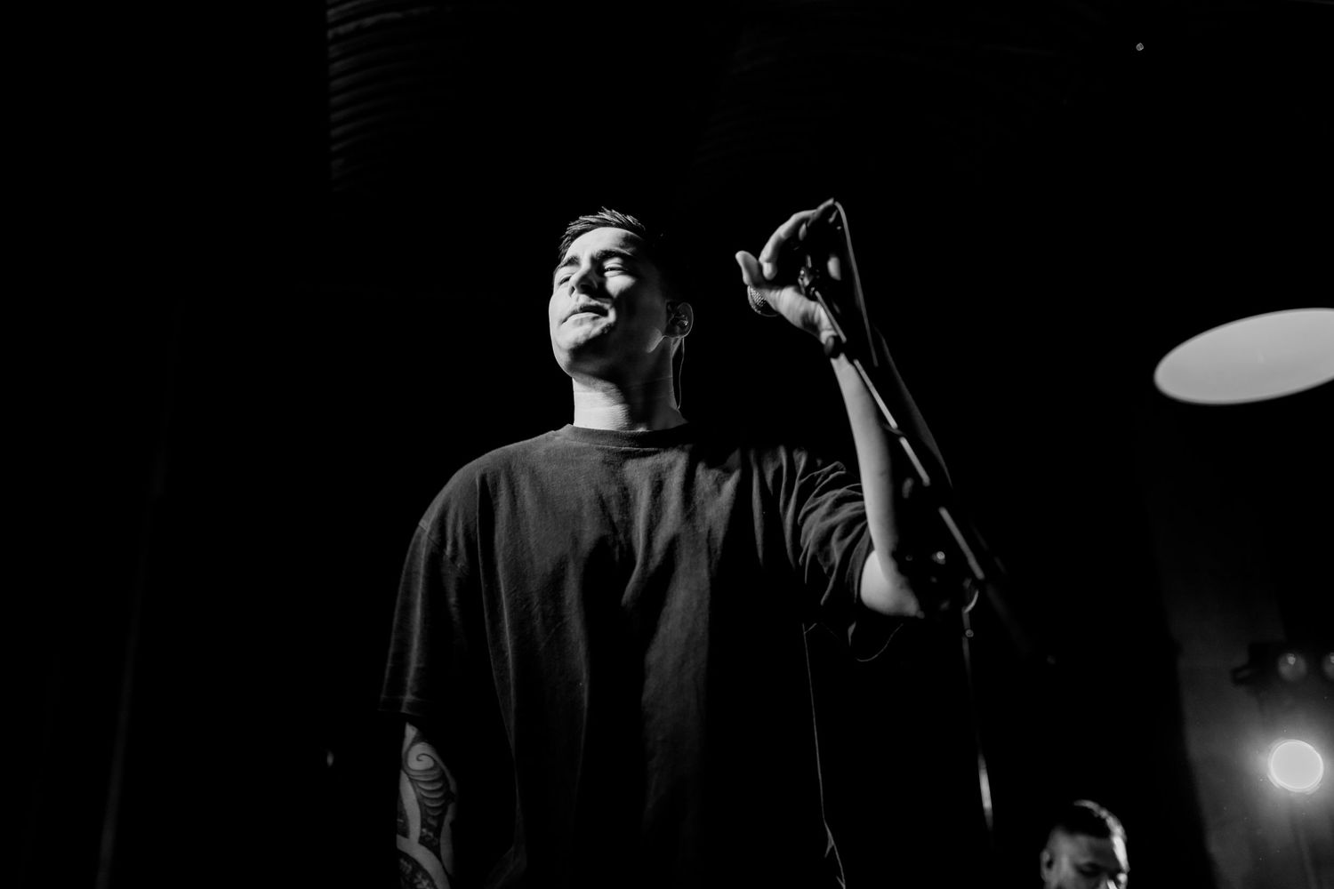 Black and white portrait of a performer singing on stage with dramatic overhead lighting.