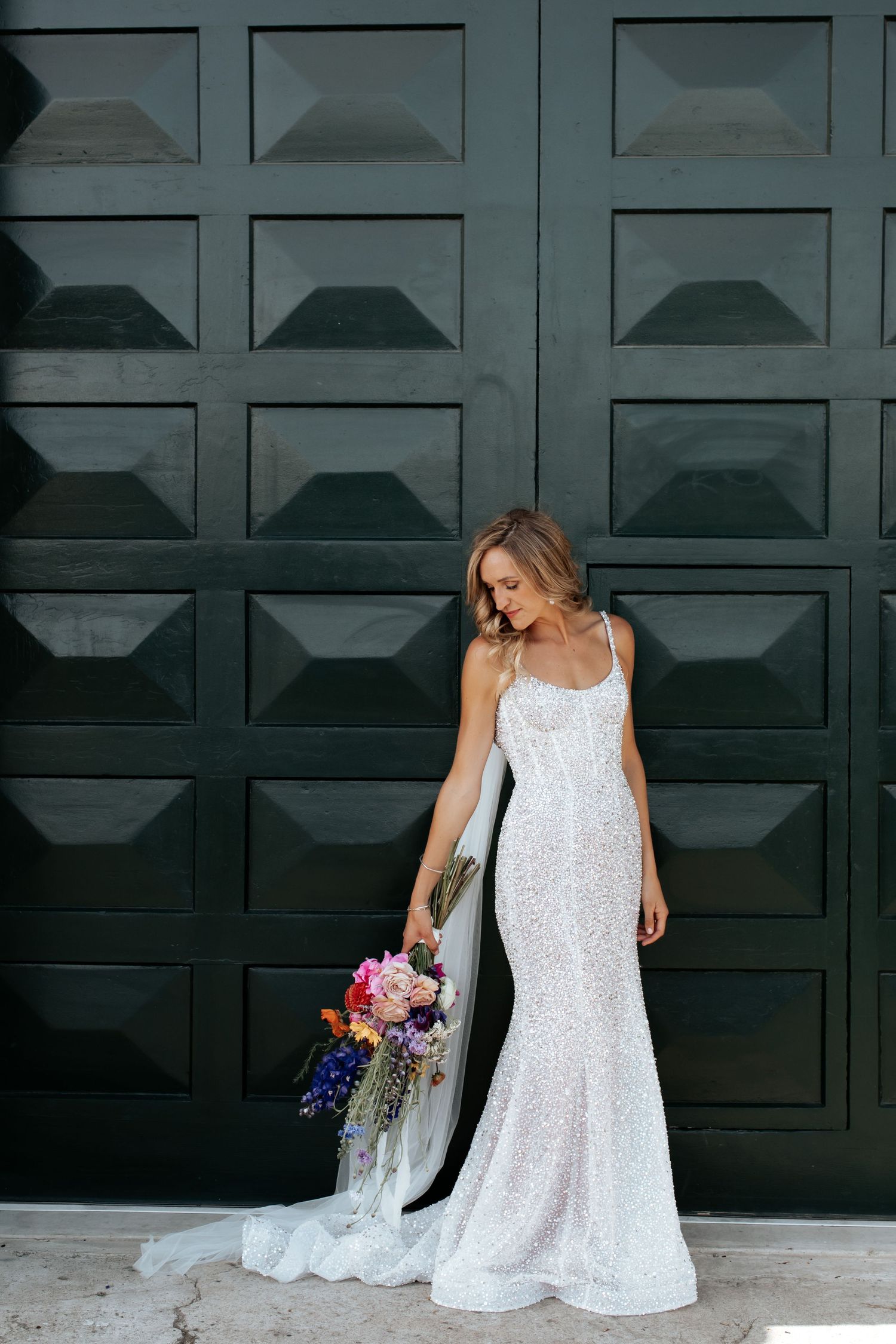 A bride in a sequined gown holds a colorful bouquet against a modern geometric backdrop.