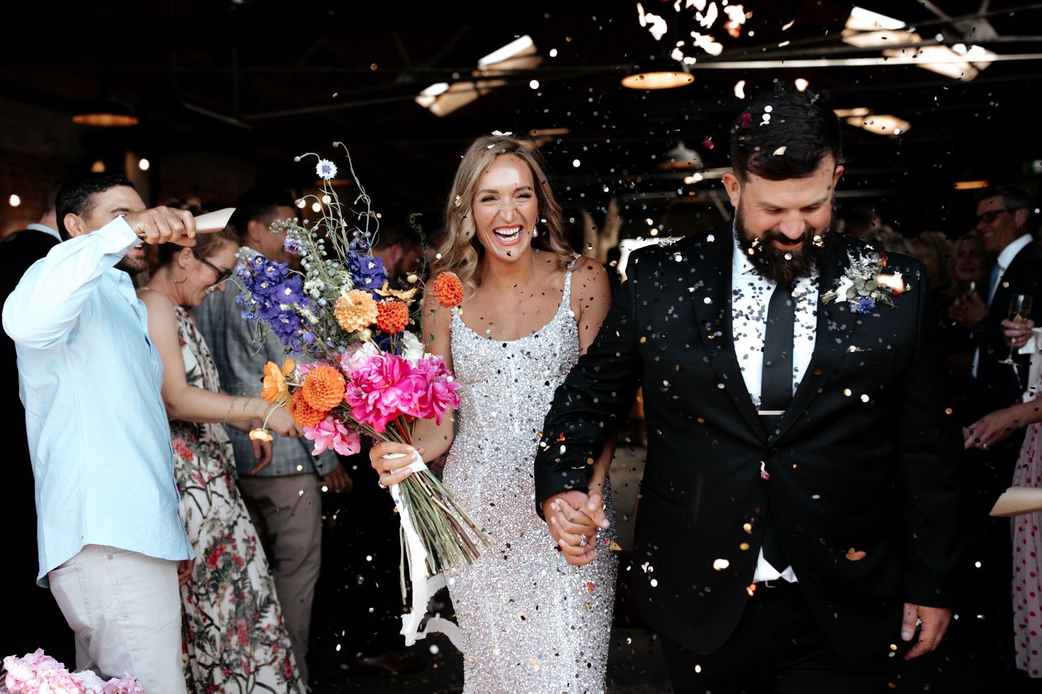 Joyful wedding exit with confetti shower and bright floral bouquet in industrial space.