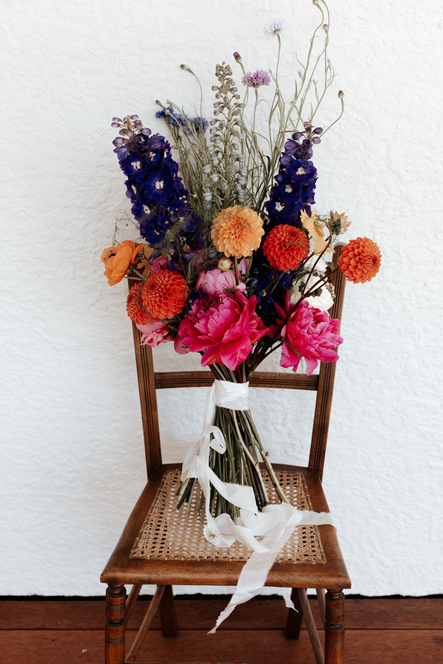 Wedding bouquet with orange and purple flowers displayed on wooden cane chair.