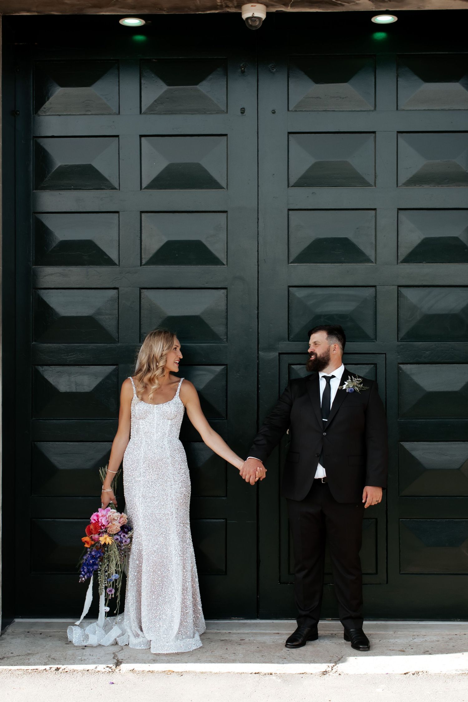 A bride and groom share a romantic moment against a geometric black door background.