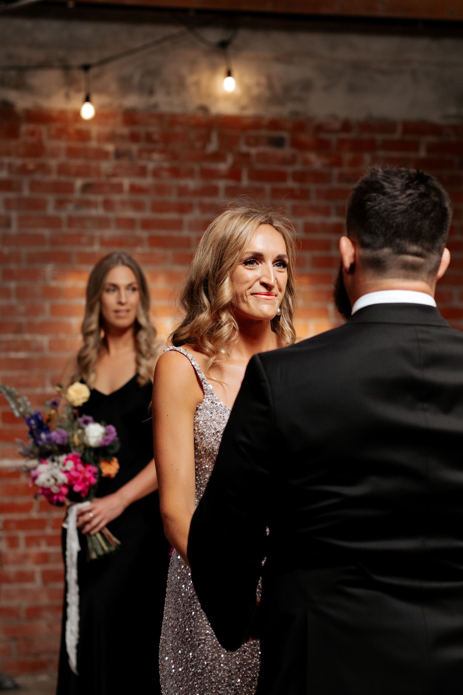Elegant wedding ceremony in industrial brick venue with sparkly dress and moody lighting.