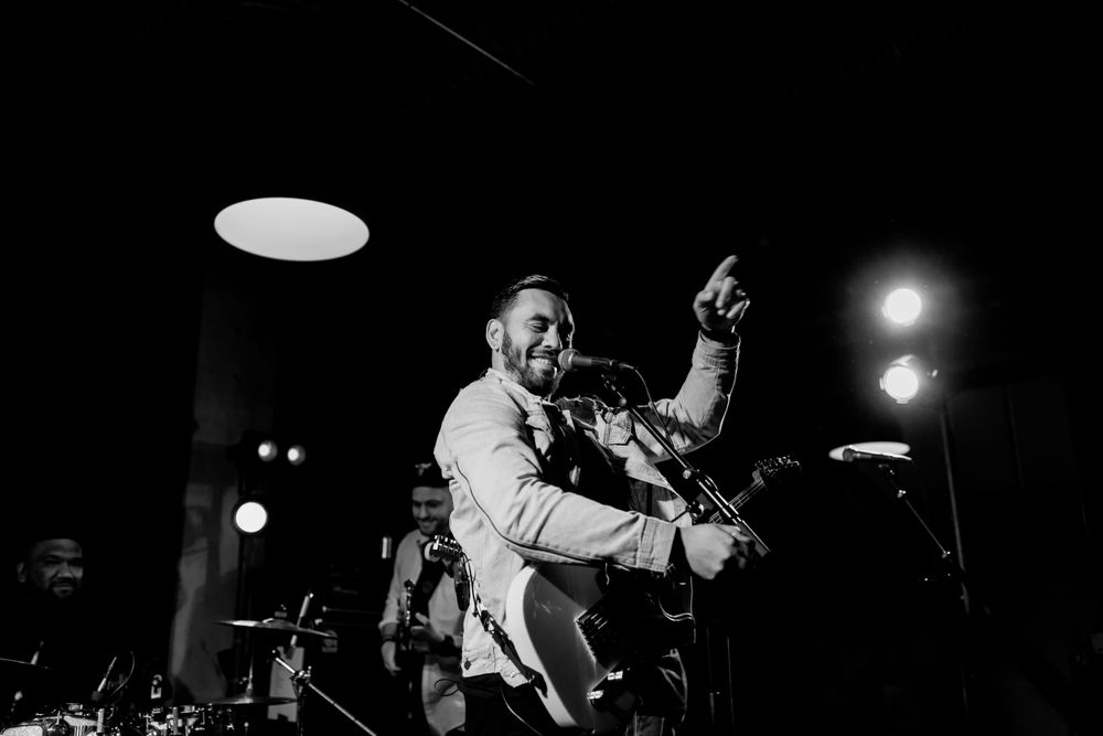 Energetic musician performing on stage in black and white with dramatic lighting.