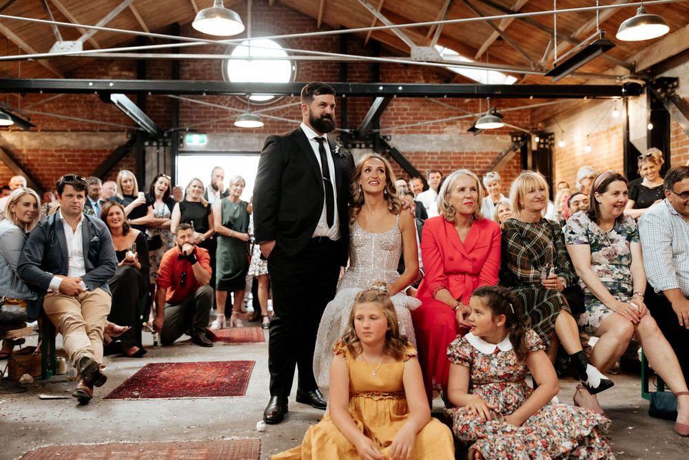 Wedding ceremony guests gather in an industrial-style venue with exposed brick walls and pendant lighting.
