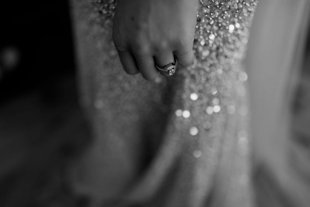 Artistic black and white detail shot of sparkly dress fabric and ring.