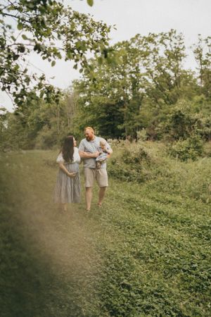 A couple spends time together on a nature path surrounded by lush green trees and foliage on a summer day.