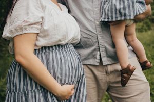 Expectant couple with toddler showing pregnancy belly in casual outdoor setting.