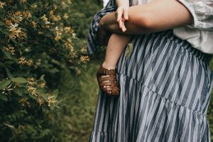 Close-up detail of a striped dress and brown leather sandals against a natural green background.