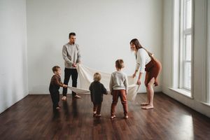 Family playing together on hardwood floors in a bright white room.