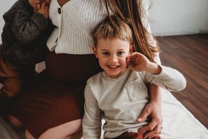 Child smiling while sitting on hardwood floor in a bright room.