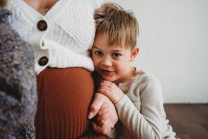 Young child in gray sweater smiling while sitting on hardwood floor.