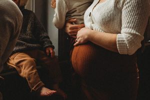A close-up view of a pregnant belly in a brown knit dress with hands gently touching.