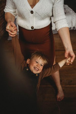 A joyful moment captured showing small legs running across a hardwood floor next to a brown skirt.